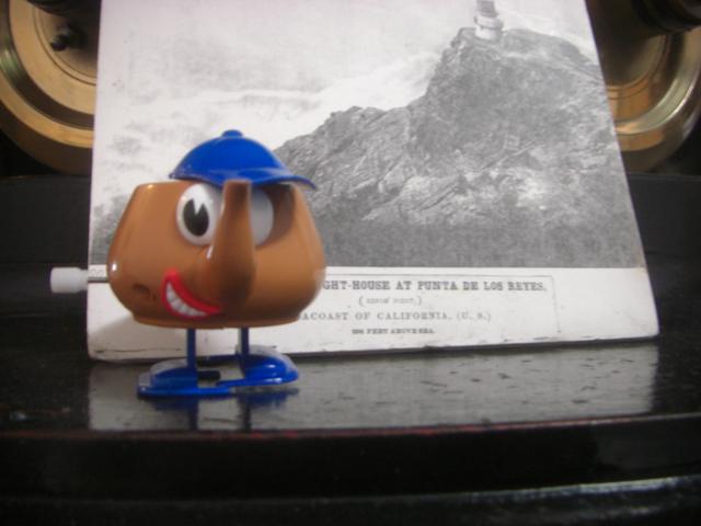 A small walking Pixar teapot inside the Point Reyes lighthouse in front of a picture depicting the "Punta des Los Reyes" lighthouse.